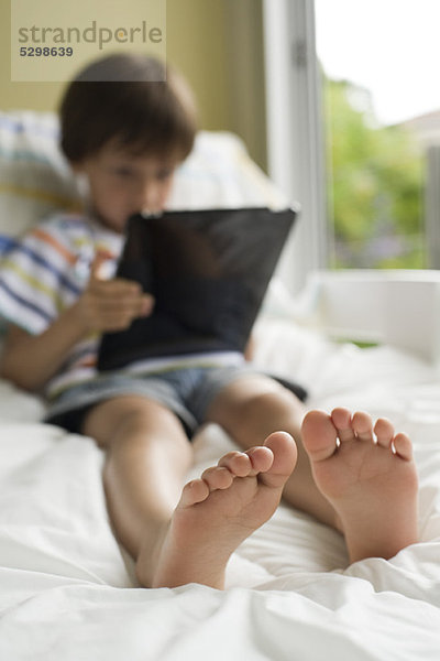 Junge entspannt auf dem Bett mit digitalem Tablett