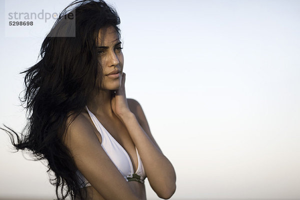 Frau im Bikini schaut weg  während langes schwarzes Haar im Wind weht  Taille oben