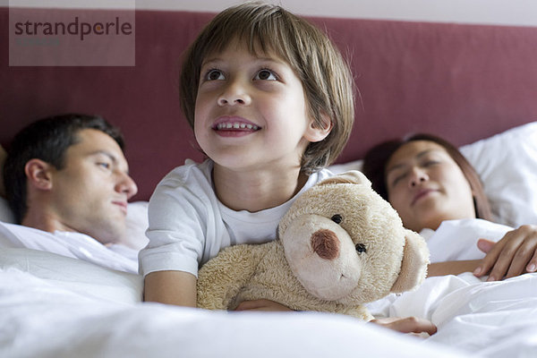 Junge im Bett der Eltern sitzend  Teddybär umarmend