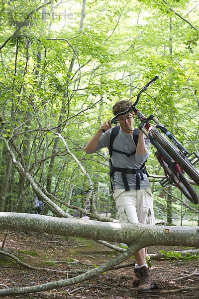 Mann mit Mountainbike im Wald mit umgestürzten Baumstämmen