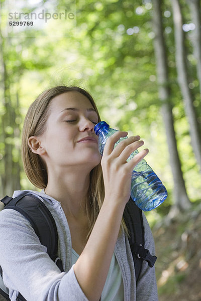 Frau trinkt Flaschenwasser im Wald