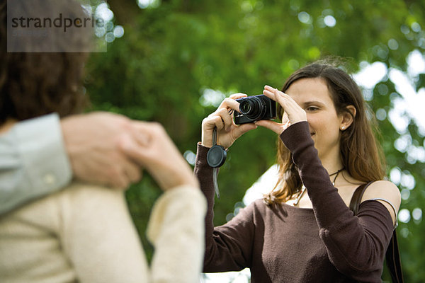 Frau fotografiert Paar mit Digitalkamera  über die Schulter gesehen