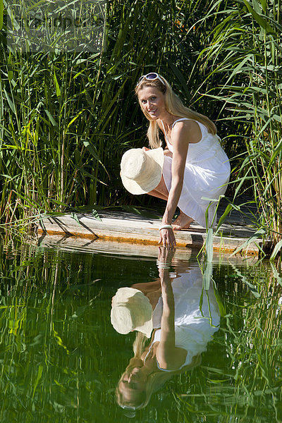 Frau hockt auf einem Holzsteg am Wasser