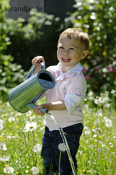 Kleiner Junge  2 Jahre  gießt mit einer Gießkanne den Garten