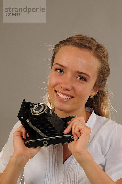 Lächelnde junge Frau mit einer alten Kamera  Balgenkamera