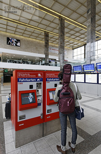 Junger Mann mit Gitarre auf dem Rücken kauft Zugticket an Fahrkarten-Automat der ÖBB  Österreichische Bundesbahnen  Westbahnhof  Wien  Österreich  Europa