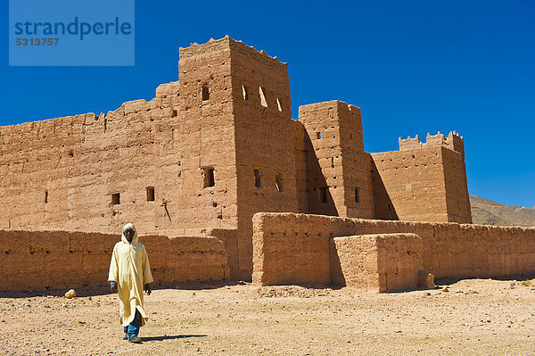 Ein Berber in traditioneller Djellabah geht vor der Kasbah Taouirt  Lehmburg  Wohnburg der Berber  Tighremt  Draa-Tal  Südmarokko  Marokko  Afrika