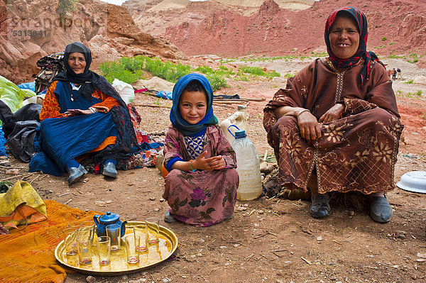Höhlennomaden  zwei Frauen und ein kleines Mädchen sitzen vor ihrer Wohnhöhle  im Vordergrund ein Messingtablett mit Teegläsern und kleiner Teekanne  Hoher Atlas  Marokko  Afrika