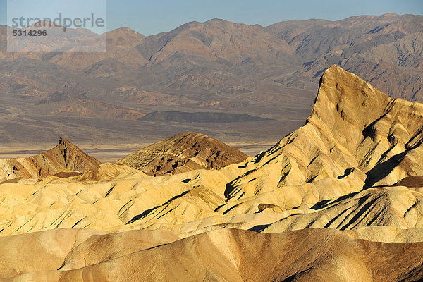 Blick von Zabriskie Point auf durch Mineralien verfärbtes erodiertes Gestein des Manly Beacon  dahinter Panamint Range  Sonnenaufgang  Death Valley Nationalpark  Mojave-Wüste  Kalifornien  Vereinigte Staaten von Amerika  USA