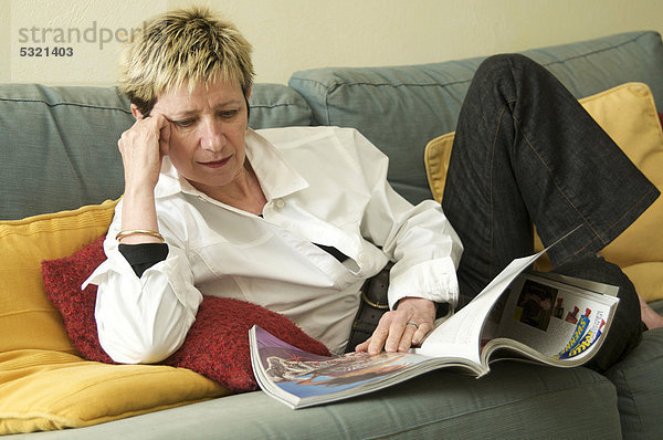Frau liegt auf einem Sofa und liest eine Zeitschrift