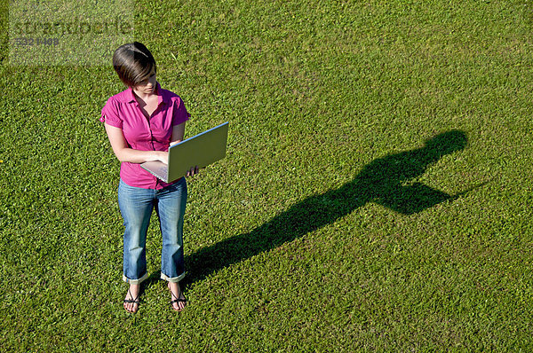 Junge Frau steht mit einem Laptop auf einem Rasen