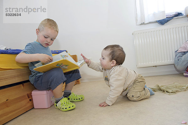 Junge  3 Jahre  blättert in einem Buch im Kinderzimmer  daneben kleiner Bruder  11 Monate