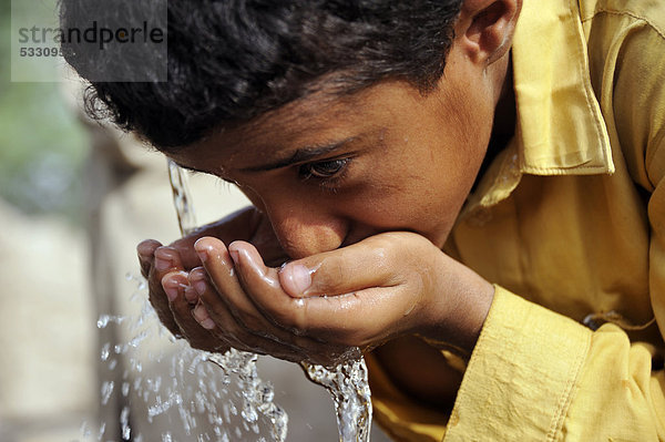 Junge  9 Jahre  trinkt Wasser an einer Brunnenpumpe  Dorf Moza Sabgogat nahe Muzaffaragarh  Punjab  Pakistan  Asien