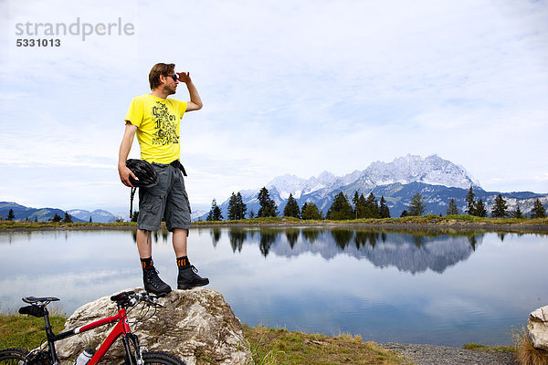 Mann mit Mountainbike auf einem Felsen schaut sich um