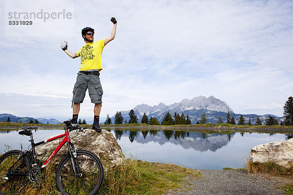 Mann mit Mountainbike posiert auf einer Felsspitze