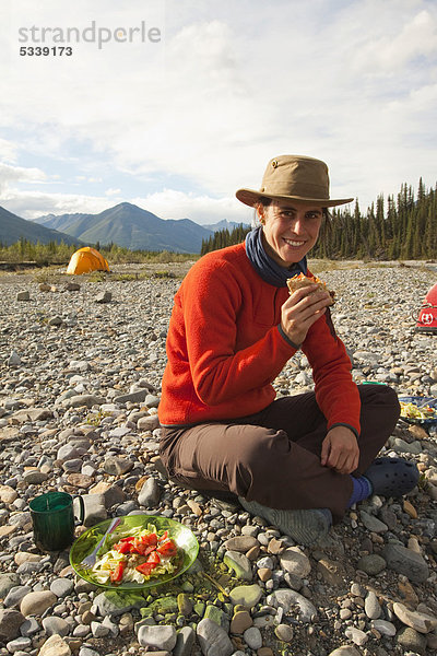 Junge Frau genießt einen Hamburger  Zelt hinten  Camping  Wind River  Yukon Territory  Kanada