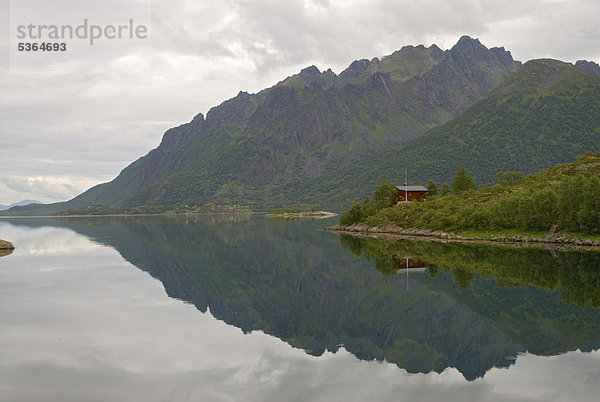 Spiegelungen von Bergen und einer roten Hütte in den ruhigen Gewässern des Sl¯verfjorden östlich von AustvÂg¯y  Lofoten  Nordland  Norwegen  Europa