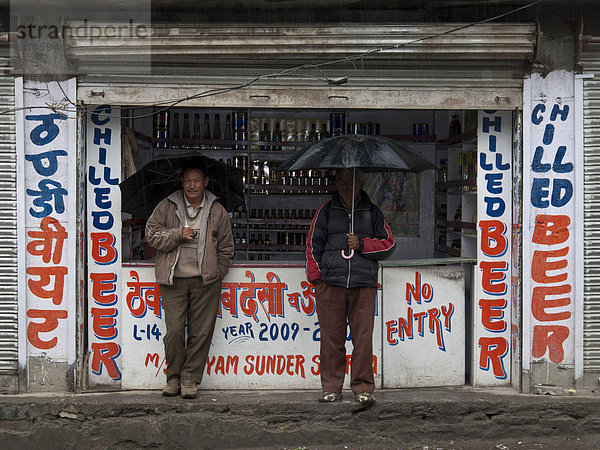 Zwei Männer haben sich in einem Alkoholladen untergestellt und warten darauf  dass der Regen aufhört  Sissu  Himachal Pradesh  Indien  Asien