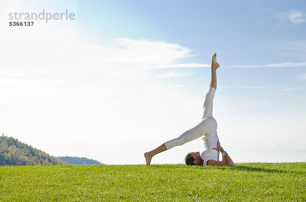 Junge Frau praktiziert Hatha-Yoga im Freien  zeigt die Stellung sarvangasana  ardha halsasana  Schulterstand  halber Pflug  Nove Mesto  Okres Teplice  Tschechische Republik  Europa