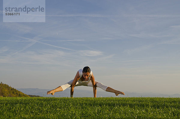 Junge Frau praktiziert Hatha-Yoga im Freien  zeigt die Stellung kakasana  bakasana  Variation von Krähe  Kranich  Nove Mesto  Okres Teplice  Tschechische Republik  Europa