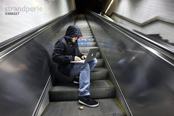 Hacker mit Laptop auf einer Rolltreppe  nachts  in einem U-Bahn-Zugang  Symbolbild Computerhacker  Computerkriminalität  Internetkriminalität  Datenklau