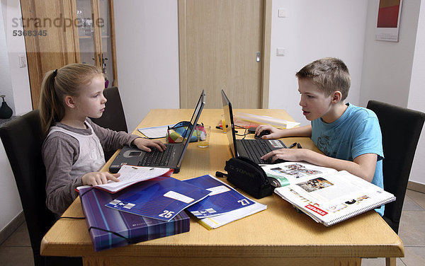 Geschwister  Bruder und Schwester mit jeweils einem Laptop  machen im Wohnzimmer gemeinsam Hausaufgaben