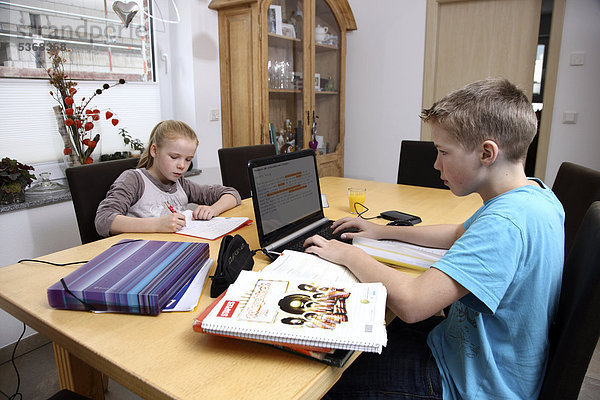 Geschwister machen im Wohnzimmer gemeinsam Hausaufgaben  Junge arbeitet mit einem Laptop Computer