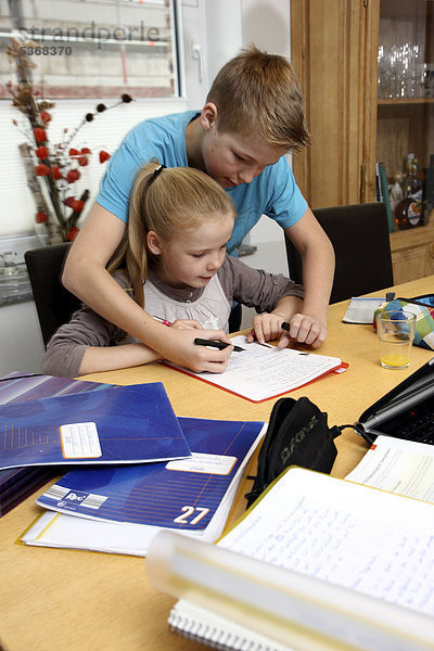 Geschwister machen im Wohnzimmer gemeinsam Hausaufgaben  Bruder hilft der Schwester bei den Schulaufgaben