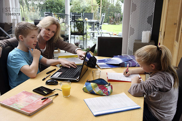 Geschwister machen im Wohnzimmer gemeinsam Hausaufgaben  mit Hilfe der Mutter