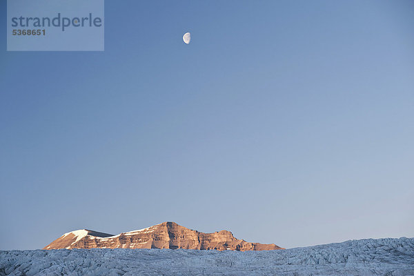 Mond steht über dem von Sonnenuntergang rot erleuchteten Nunatak Terrierfjellet im Nordenskiöldbreen  Billefjord  Spitzbergen  Norwegen  Skandinavien  Europa