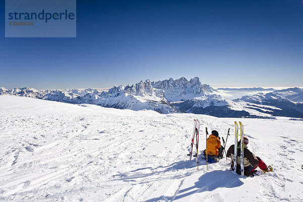 Skitourengeher machen Rast auf dem Gipfel vom Uribrutto oberhalb vom Passo Valles  hinten die Pallagruppe und der Passo Rolle  Trentino  Dolomiten  Italien  Europa