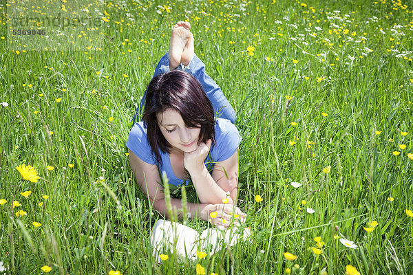 Junge Frau liegt im Gras und liest ein Buch