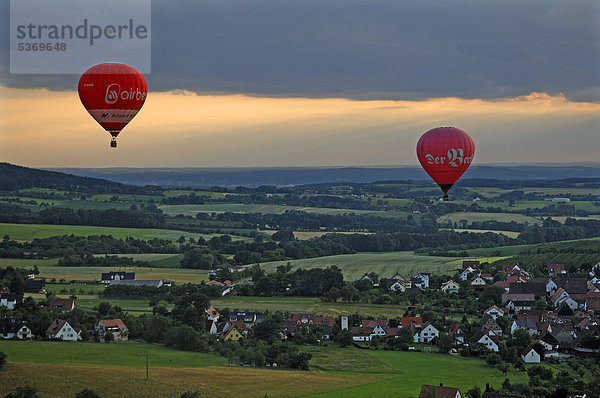 Zwei Heißluftballons am Abendhimmel über einem fränkischen Dorf  Weingarts  Oberfranken  Bayern  Deutschland  Europa