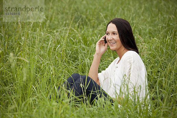 Junge Frau sitzt im hohen Gras  telefoniert