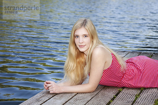 Junge Frau liegt entspannt auf einem Steg am Wasser
