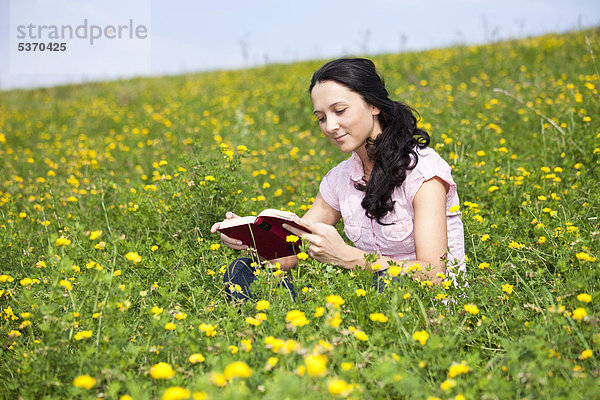 Junge Frau sitzt auf einer Wiese  liest ein Buch