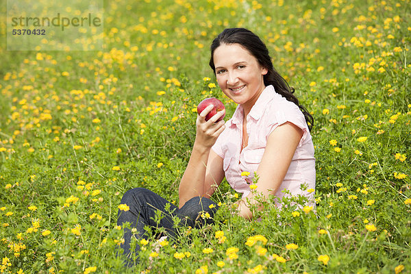 Junge Frau sitzt auf einer Wiese  isst einen Apfel