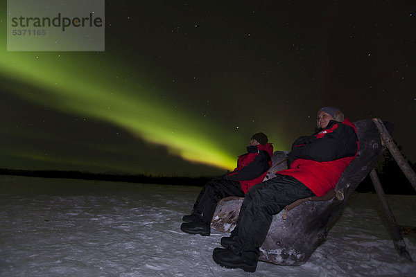 Junges Paar  Frau und Mann  beim Schneeschuhwandern  beobachten wirbelnde grüne nördliche Polarlichter  Aurora borealis  bei Whitehorse  Yukon Territory  Kanada  Amerika