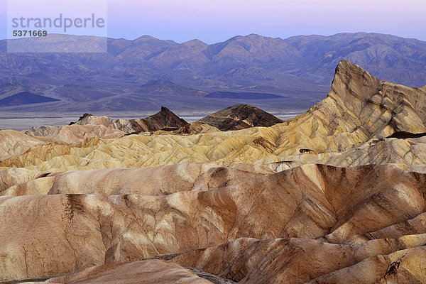 Blick von Zabriskie  auch Zabriske Point  auf durch Mineralien verfärbtes erodiertes Gestein des Manly Beacon  dahinter Panamint Range  Morgendämmerung  Death Valley Nationalpark  Mojave-Wüste  Kalifornien  Vereinigte Staaten von Amerika  USA