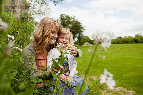 Mutter und Tochter sitzen im Feld mit Wildblumen