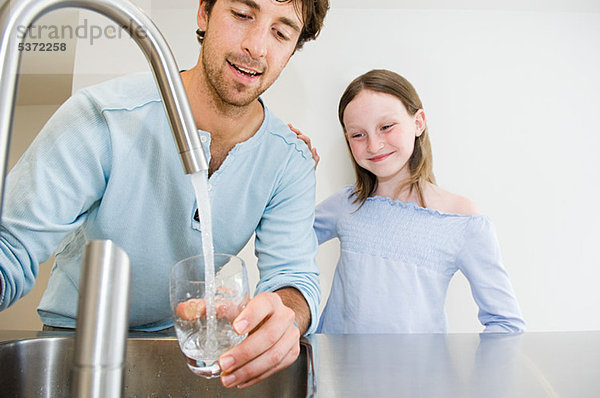 Junger Mann füllt ein Glas Wasser für Tochter