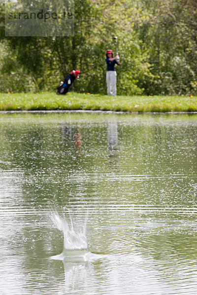 Person  die den Golfball ins Wasser schlägt