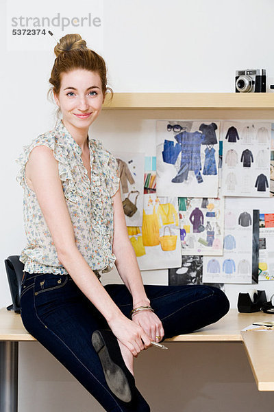 Junge Modedesignerin auf dem Schreibtisch sitzend  Portrait