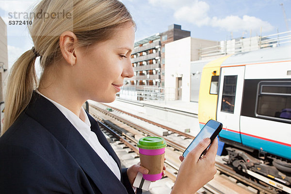 Geschäftsfrau mit Kaffee und Smartphone im Bahnhof