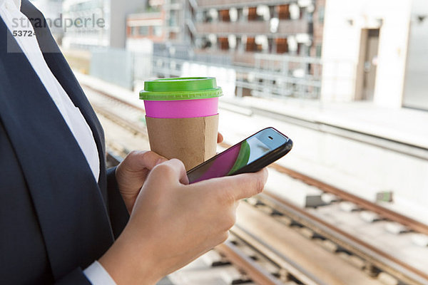 Nahaufnahme der Frau mit Kaffee und Smartphone im Bahnhof