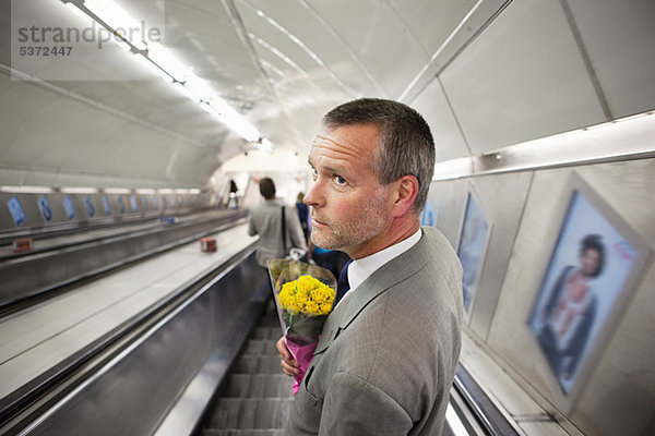 Mann auf U-Bahn Rolltreppe mit Blumen