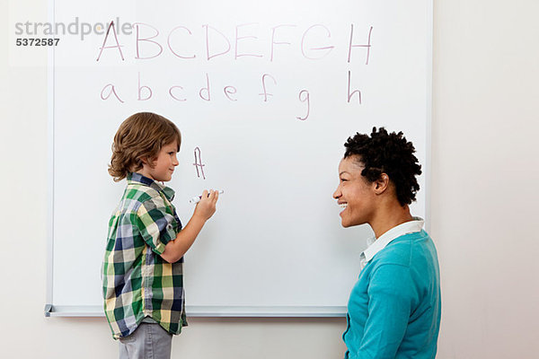 Lehrer und junge Alphabet auf Whiteboard schreiben