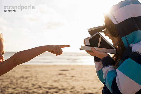 Mädchen zeigt auf Freundin mit Sofortbildkamera am Strand