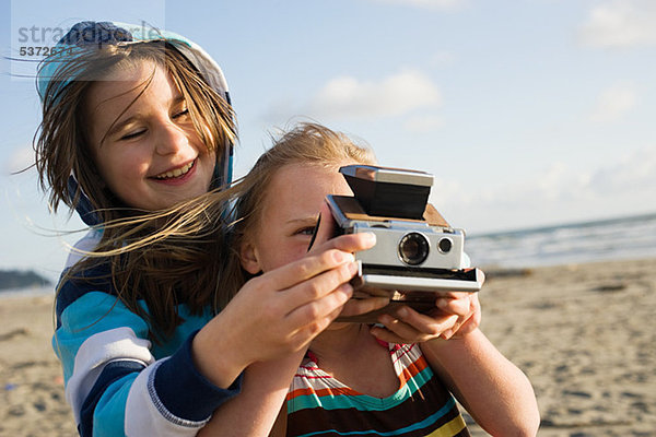 Mädchen zeigt Freundin  wie man eine Sofortbildkamera am Strand benutzt.