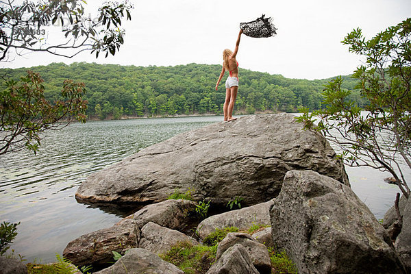 Young Woman holding Decke auf Felsen am See